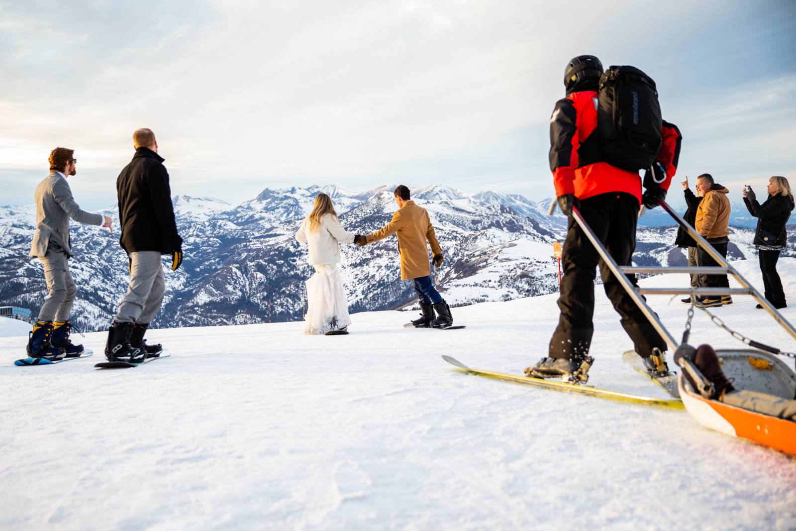 Bride and groom snowboard down a mountain at sunset