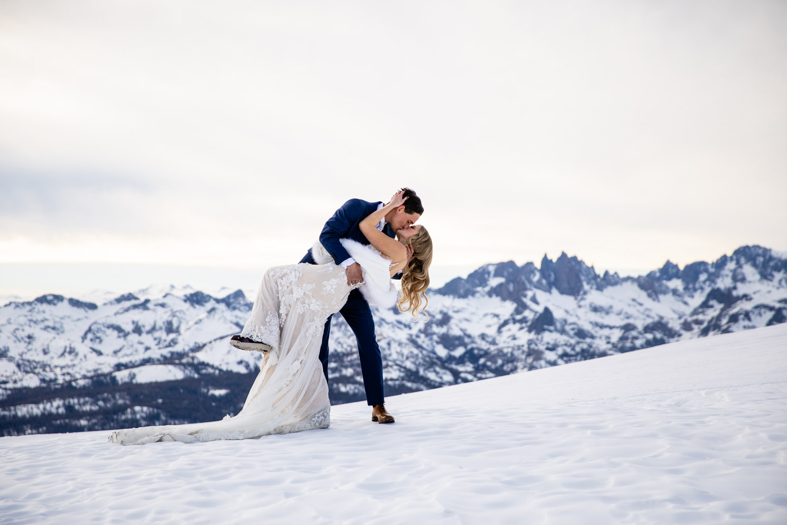 Groom dips and kisses bride on Mammoth Mountain with the Eastern Sierra mountains